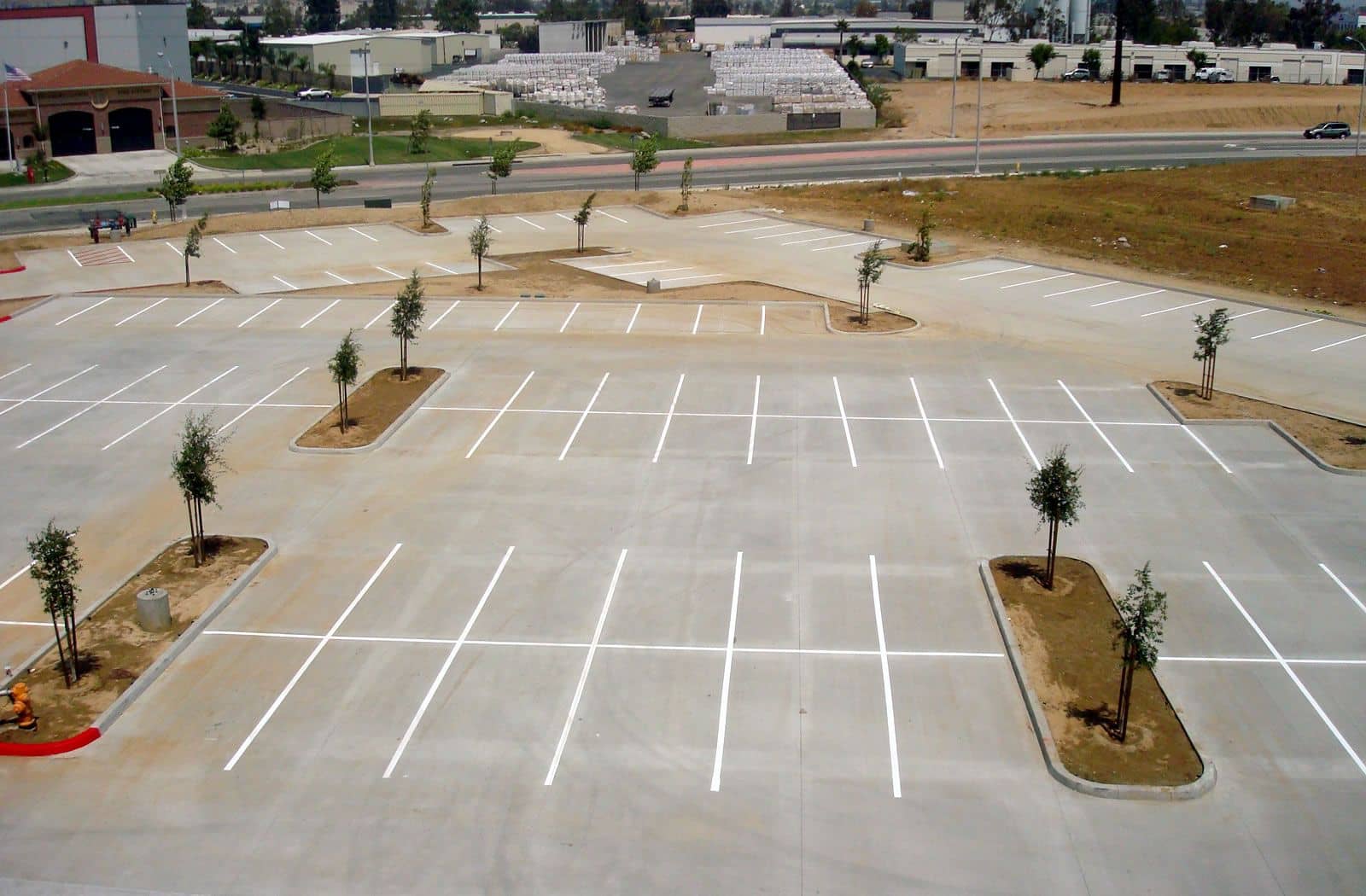 Elevated view of a large, light-gray new parking lot with crisp white stall striping and young trees in planter islands