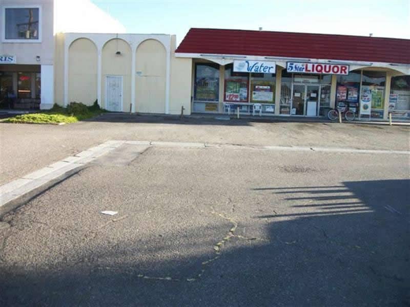 Faded, cracked asphalt parking lot in front of a small retail strip