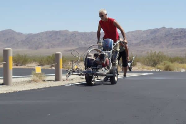 Worker pushing a line-striping machine across fresh asphalt with desert mountains behind