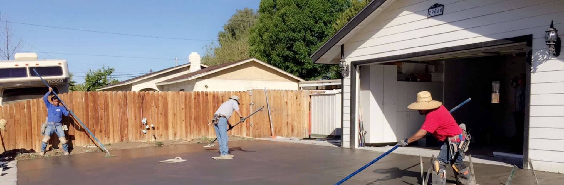 Concrete finishers working a freshly poured residential driveway slab with long-handled bull floats