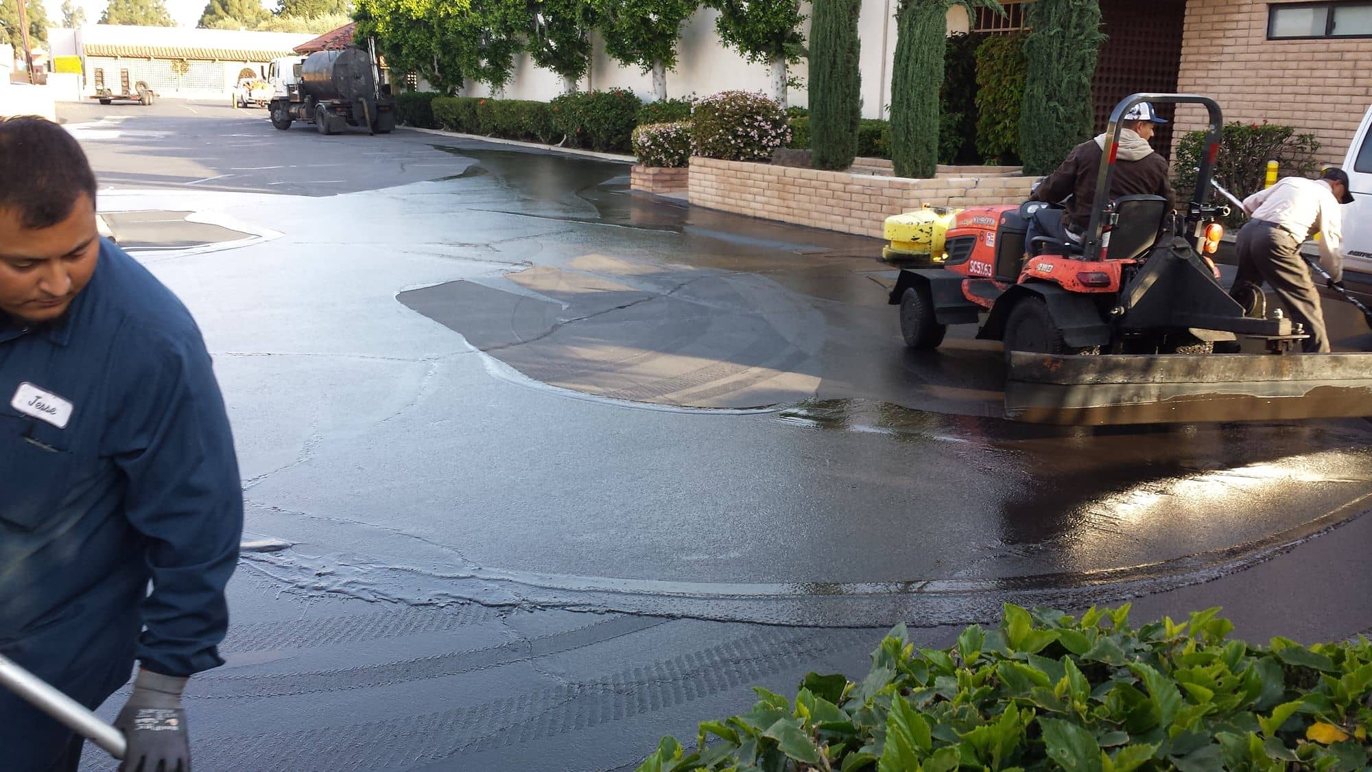 Crew member detailing sealer around landscaping while the tractor works the open lot