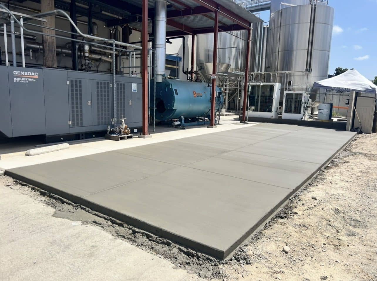New concrete equipment pad poured beside industrial tanks and a generator