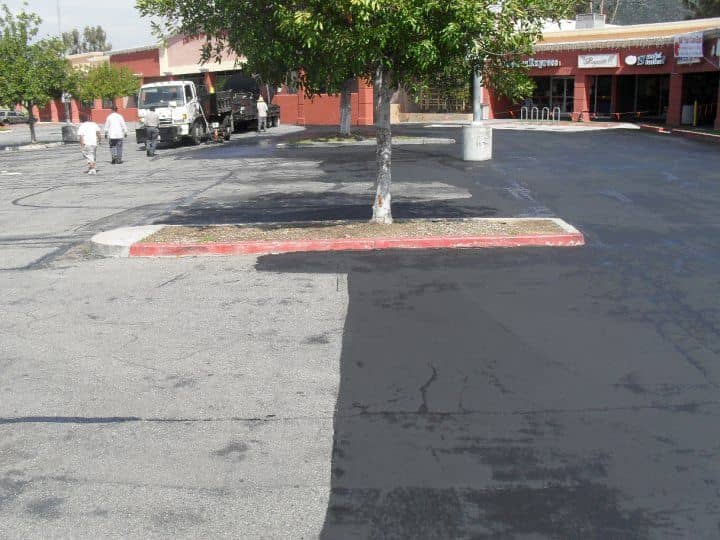One parking area split down the middle: gray, weathered asphalt on the left and fresh black sealcoat on the right