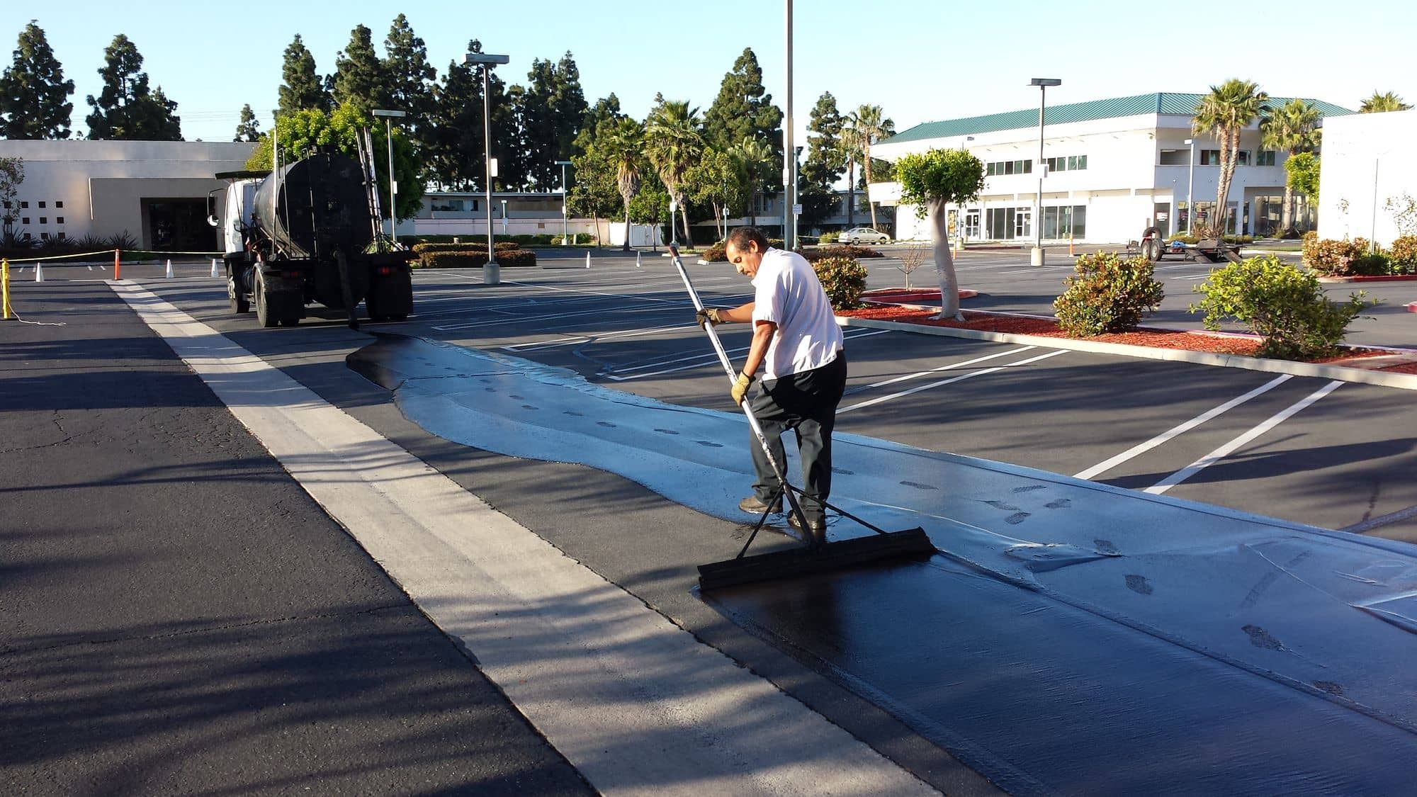 Crew member squeegeeing sealer by hand along the painted edge of a parking stall