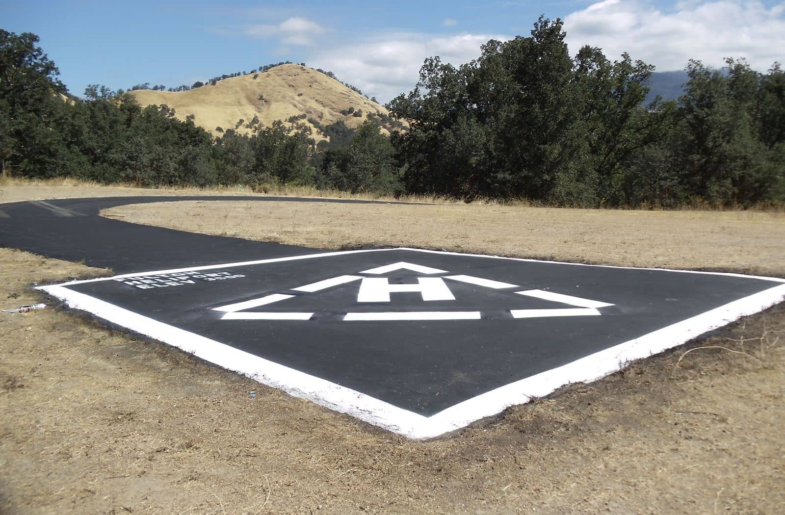 Freshly paved and painted helipad with a white H marking set against dry hills