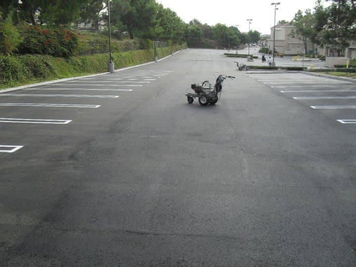 Walk-behind line-striping machine parked on a long tree-lined lot with fresh white stall lines