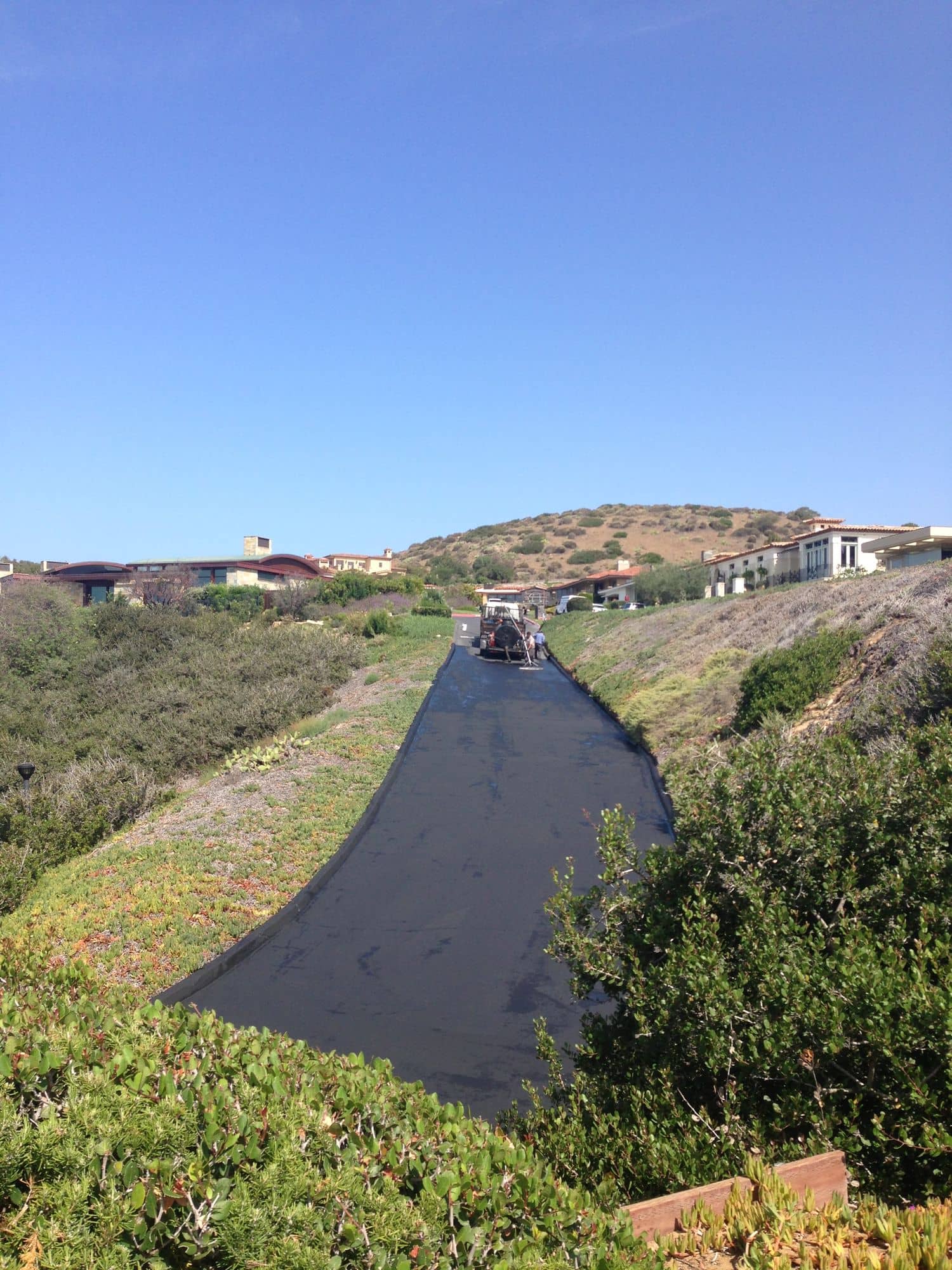 During: the hillside drive coated in fresh black sealer, with the crew working at the far end