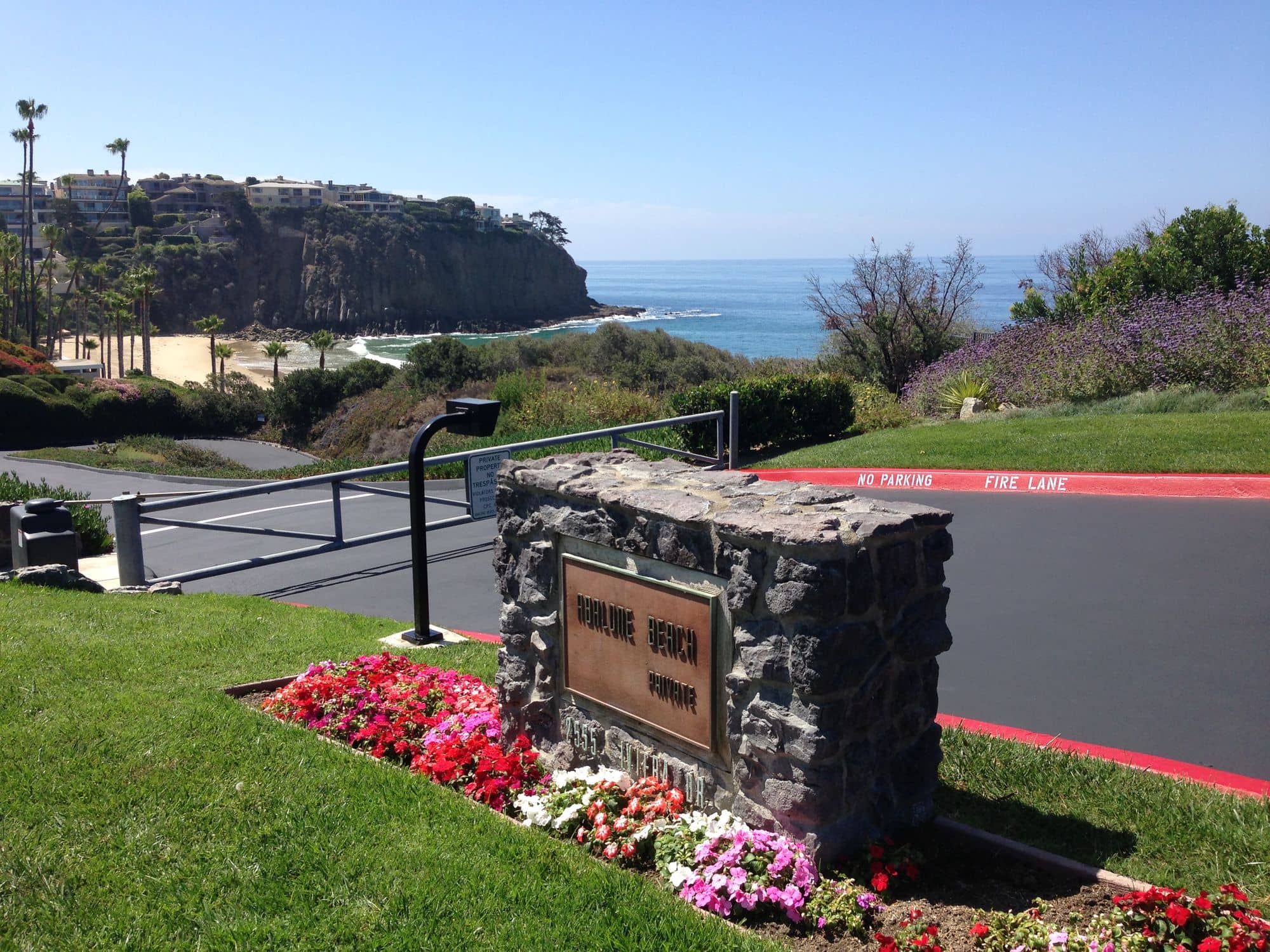 Stone entry monument and flower bed beside a freshly sealed drive with ocean views beyond