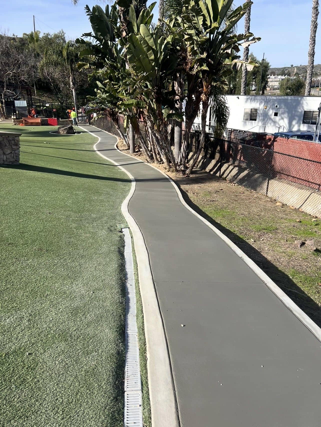 Long concrete walking path with a curb edge winding through a landscaped hillside