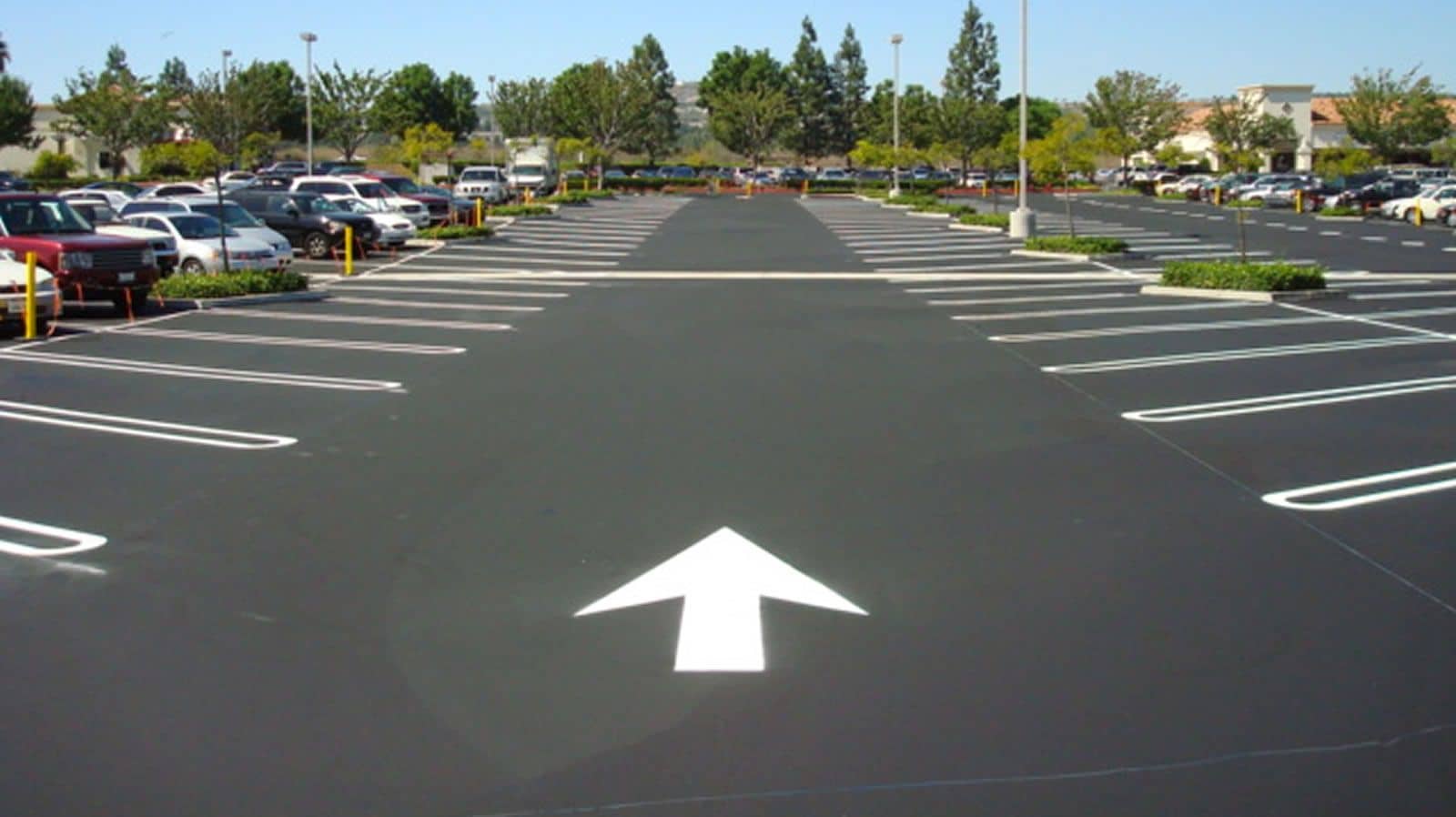 Deep black parking lot with bright white stall lines and a directional arrow