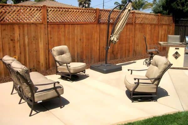 Smooth concrete backyard patio with lounge chairs beside a wooden fence