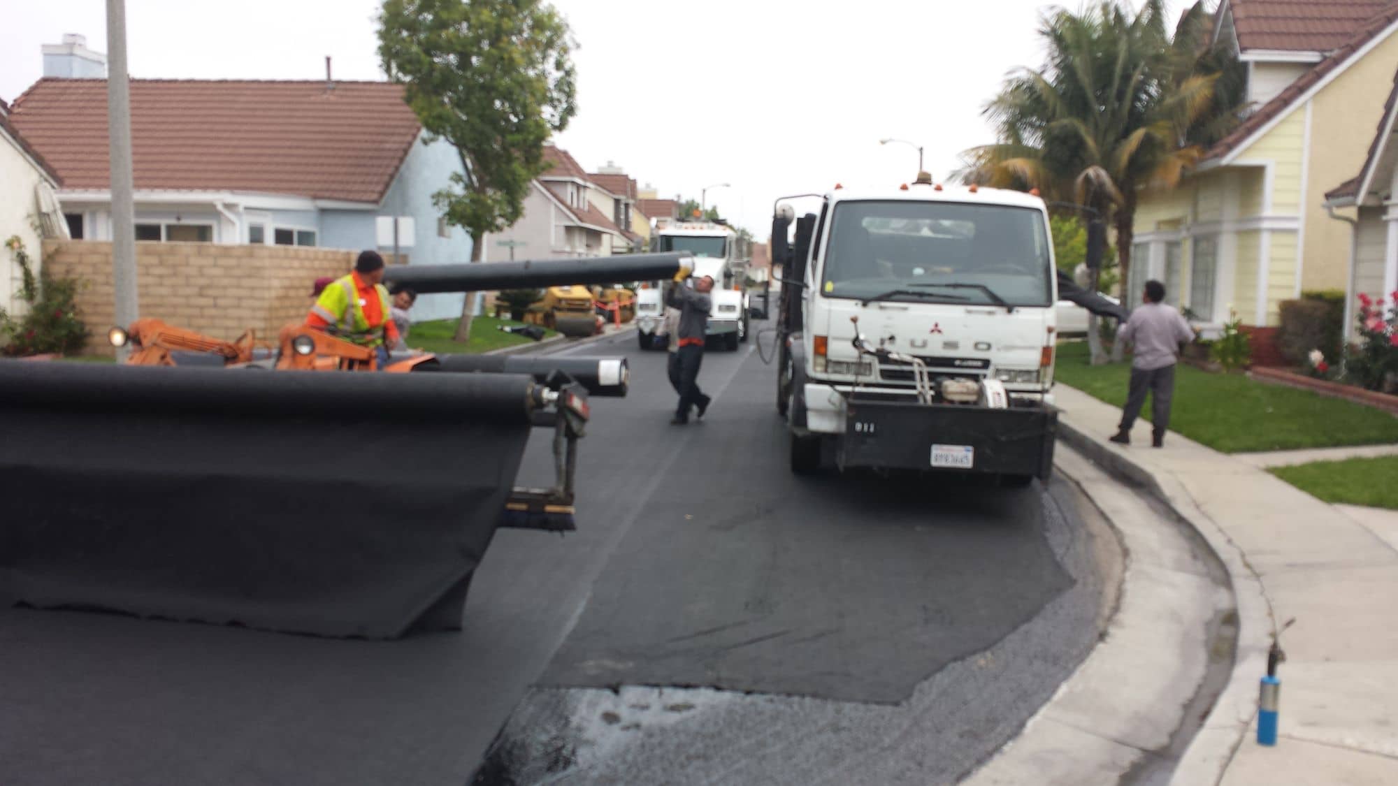 Wide roll of paving fabric being unwound from the back of a work truck across a residential street