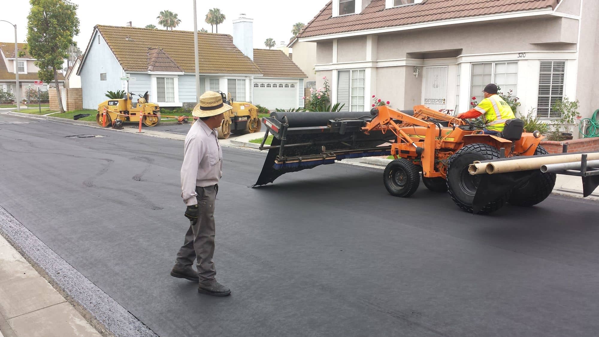 Orange tractor towing a fabric laydown rig over a freshly covered street as a crew lead walks alongside