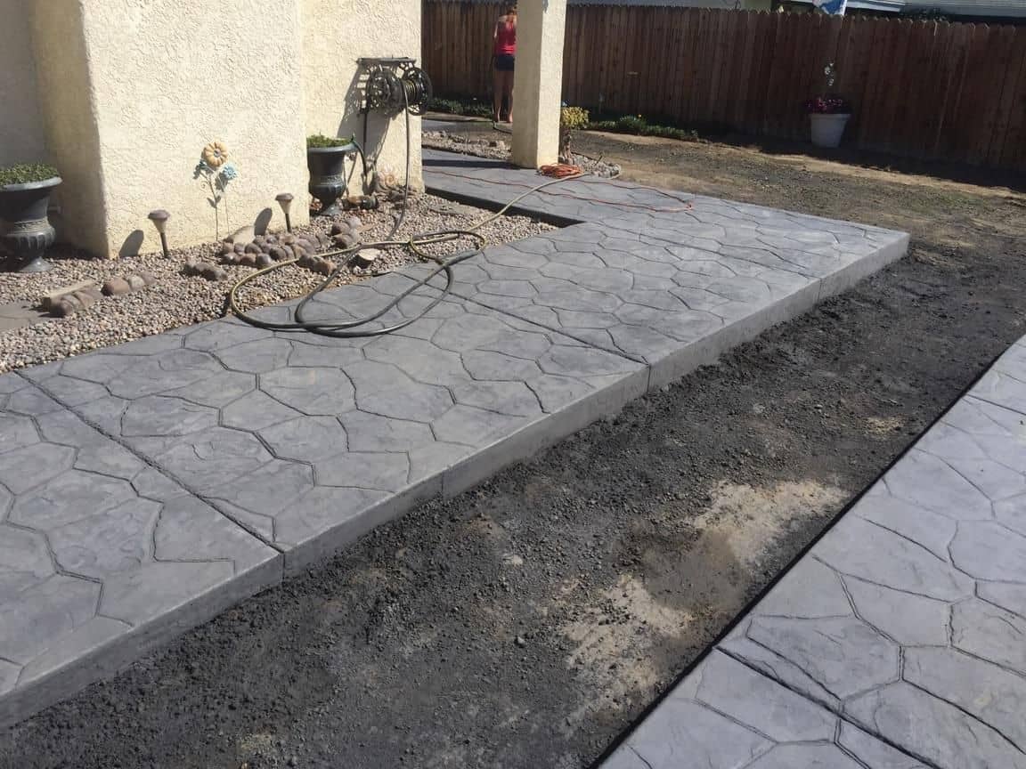 Gray stamped-concrete walkway with a stone pattern curving along a backyard planter bed