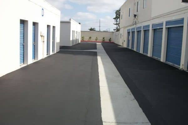 New asphalt drive aisle running between rows of self-storage units with blue roll-up doors
