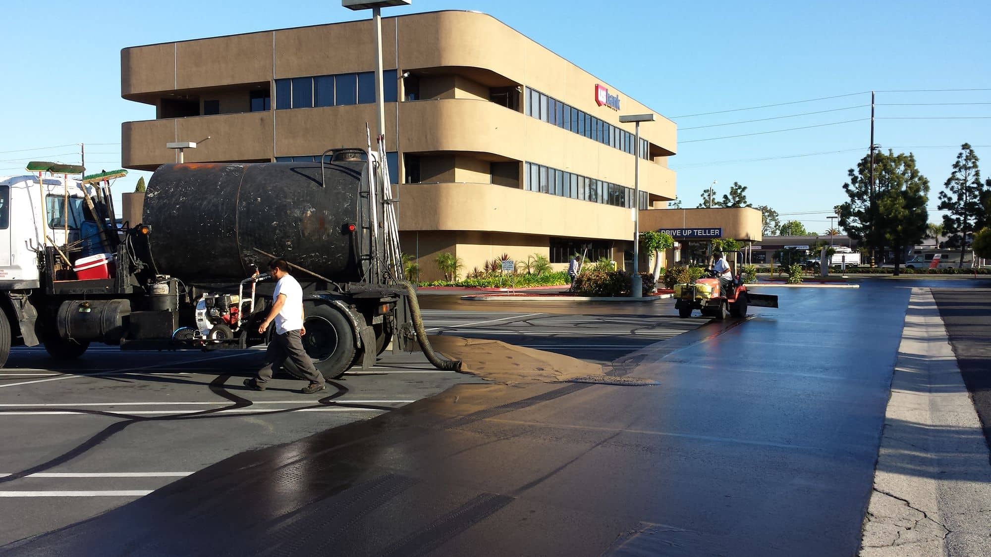 Sealcoat crew working from a tank truck in front of a three-story office building
