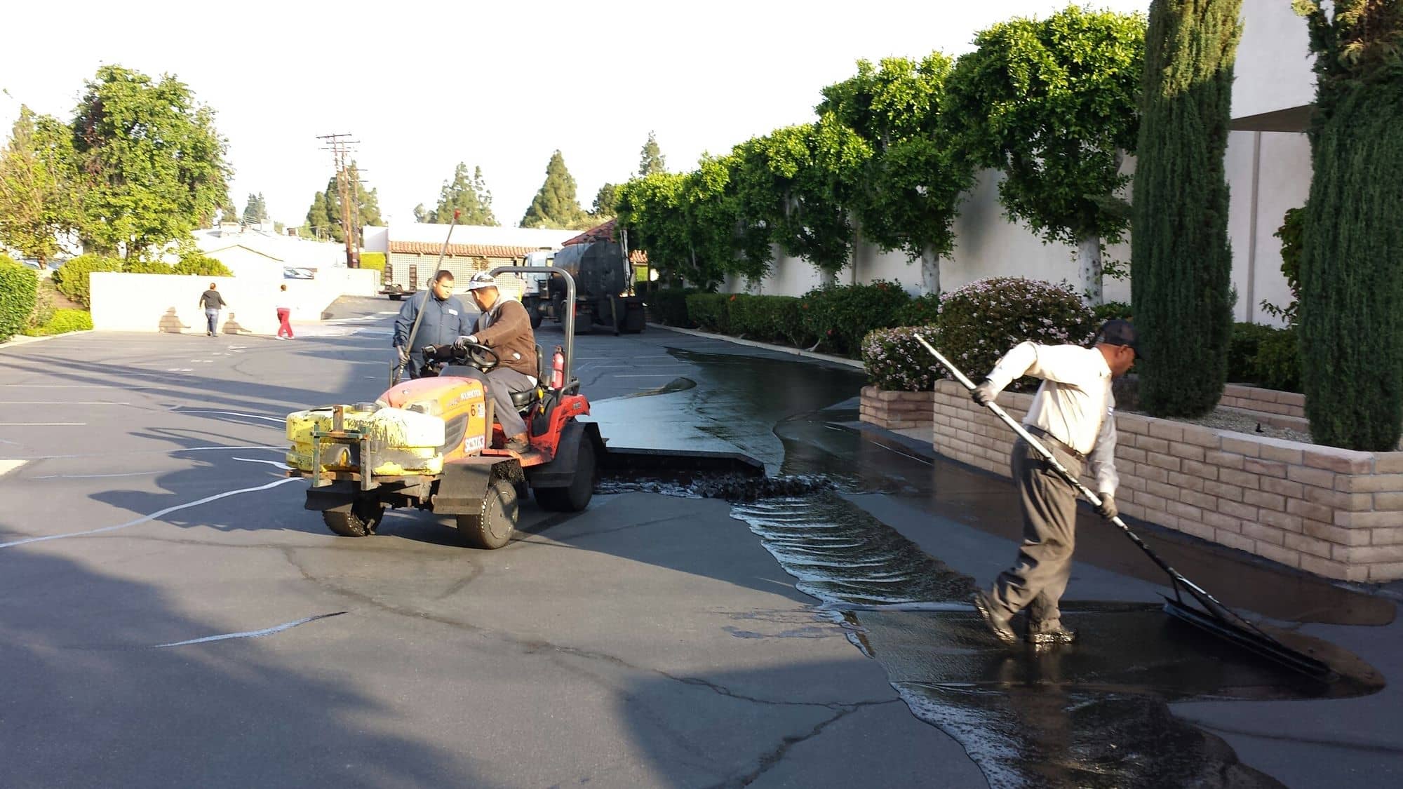 Crew applying sealer by squeegee next to a block wall as a spray rig follows