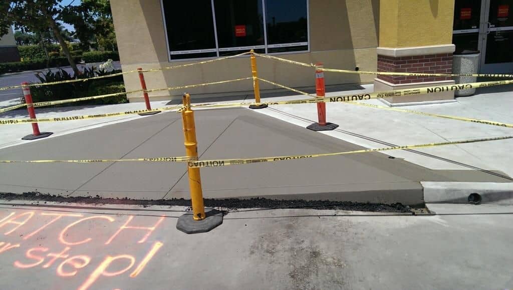 Replaced concrete walkway section behind caution tape and delineators at a building entrance