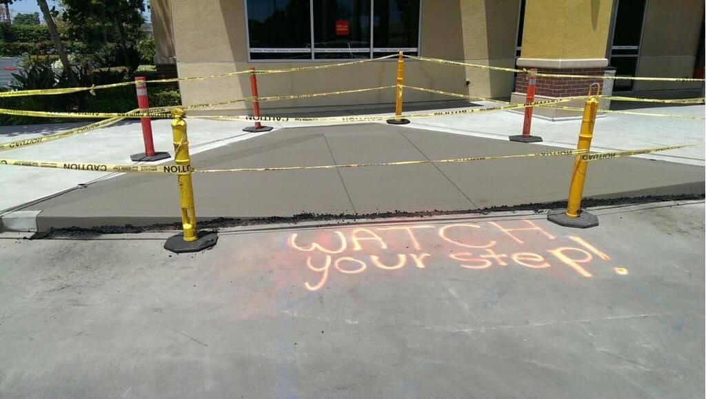 Freshly poured walkway panel surrounded by barricades with 'watch your step' chalked on the pavement