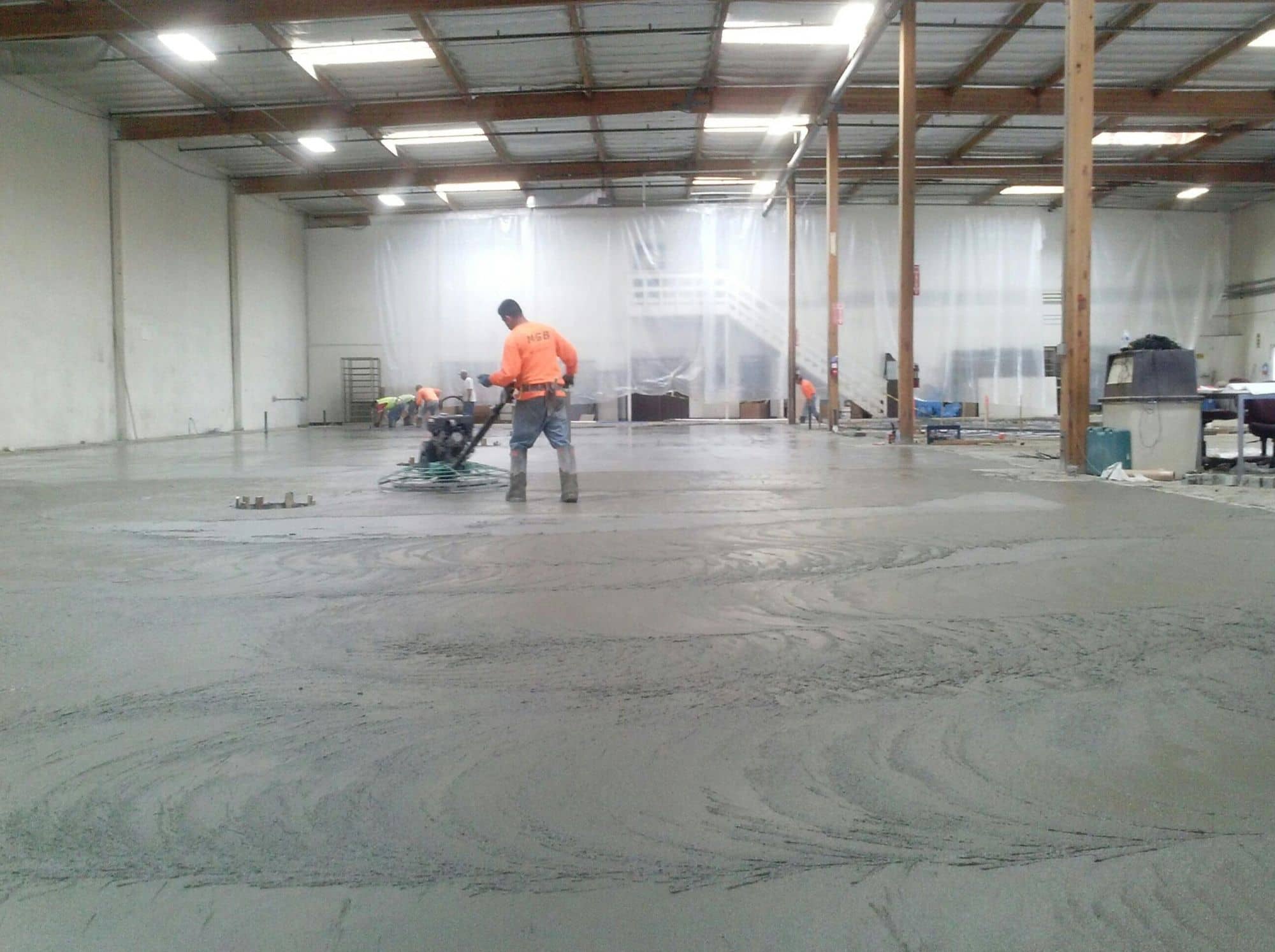 Finisher running a power trowel across a large interior warehouse slab