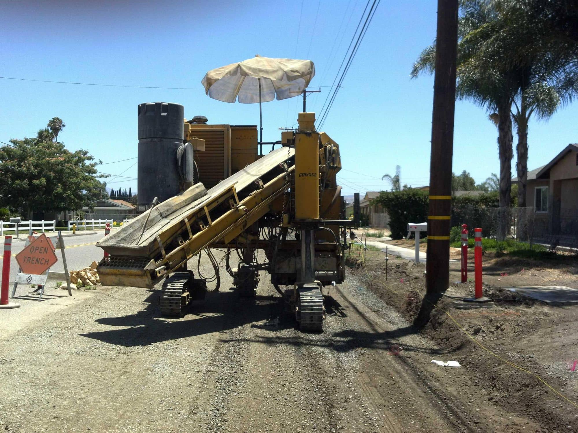 Yellow curb-and-gutter machine fed by a conveyor, extruding new curb along a street
