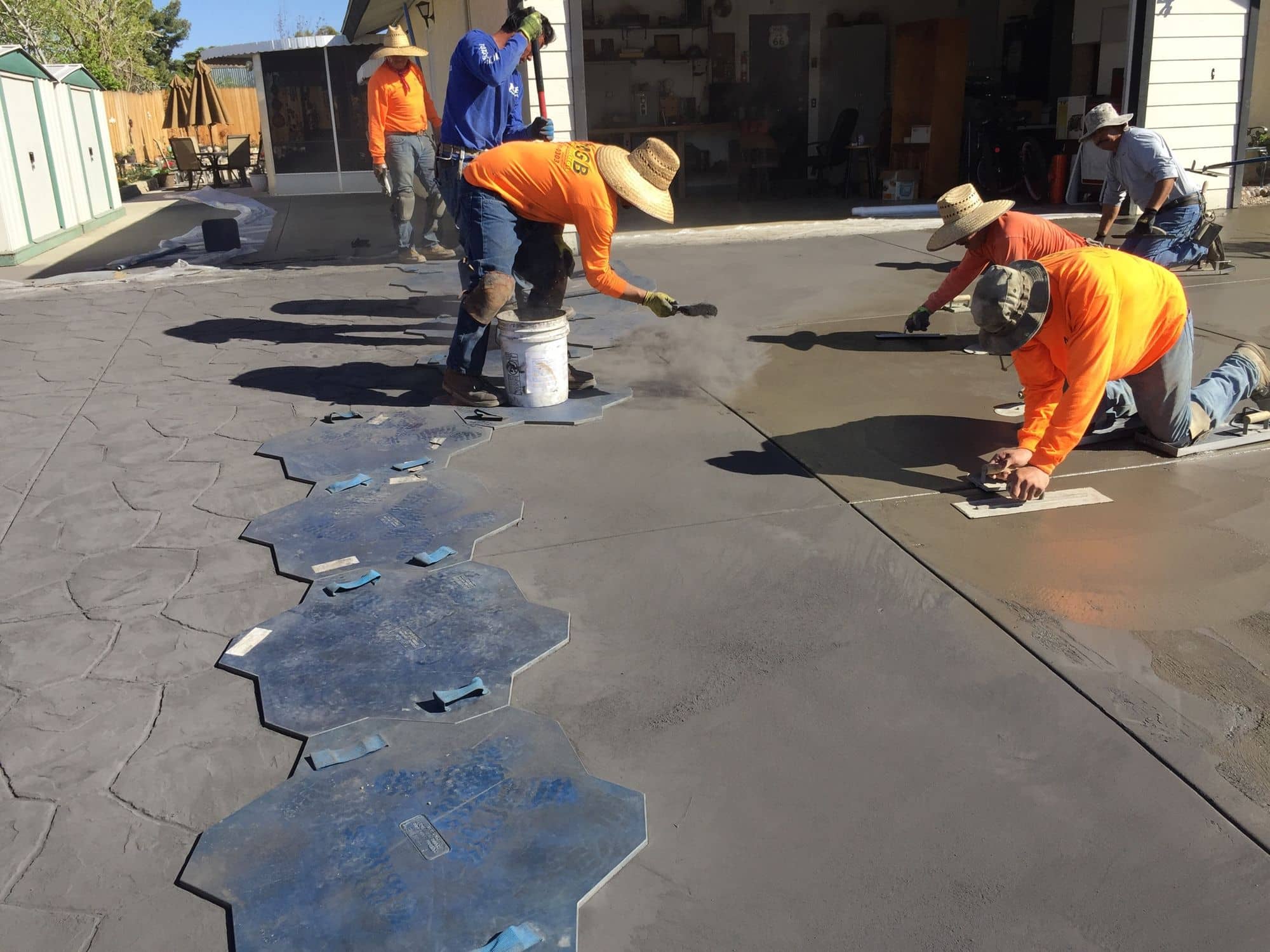 Crew kneeling on fresh concrete pressing blue stamp mats to create a patterned surface